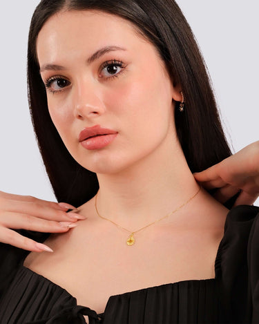 A poised model with a subtle smile wearing a 14K gold vermeil Eye of Horus necklace, black blouse with bow details.