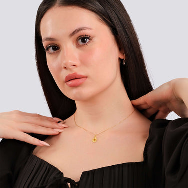 A poised model with a subtle smile wearing a 14K gold vermeil Eye of Horus necklace, black blouse with bow details.