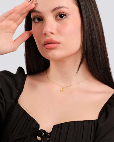 A poised model with a subtle smile wearing a 14K gold vermeil Eye of Horus necklace, black blouse with bow details.