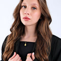 Portrait of a young woman with wavy brown hair and blue eyes, wearing a 14K gold vermeil Christian fish necklace against a black top.