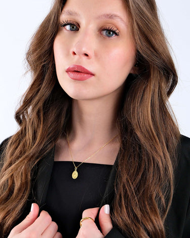 Portrait of a young woman with wavy brown hair and blue eyes, wearing a 14K gold vermeil Christian fish necklace against a black top.