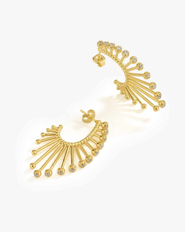 A pair of 14K gold vermeil sunburst earrings laid on a white surface, each designed with a semi-circular ridge and multiple dangling golden beads.