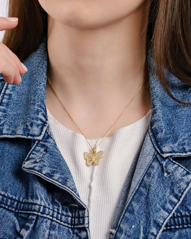 Close-up view of a woman&#39;s neck area, featuring an 18K gold vermeil butterfly necklace on a thin gold chain, set against a white top and a blue denim jacket.