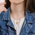 Close-up view of a woman&#39;s neck area, featuring an 18K gold vermeil butterfly necklace on a thin gold chain, set against a white top and a blue denim jacket.