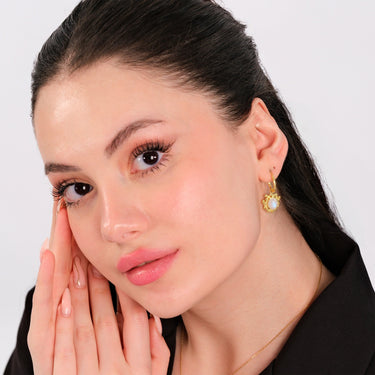 A young woman with her hair pulled back, wearing 14K gold vermeil moonstone earrings, the intricate sunburst design around the moonstone complementing her subtle makeup and black outfit.