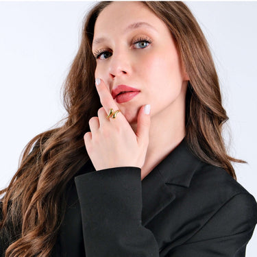 Portrait of a young woman with long brown hair wearing a black blazer and a gold snake ring, her hand touching her chin thoughtfully.