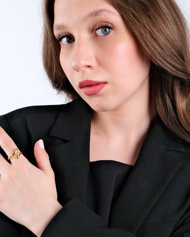 Young woman with blue eyes and brunette hair wearing a black blazer and a gold snake ring, gazing directly at the camera