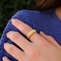 A close-up of a woman&#39;s hand with neatly manicured nails, wearing a 14k gold vermeil croissant ring on her middle finger, resting on a knitted blue sweater.