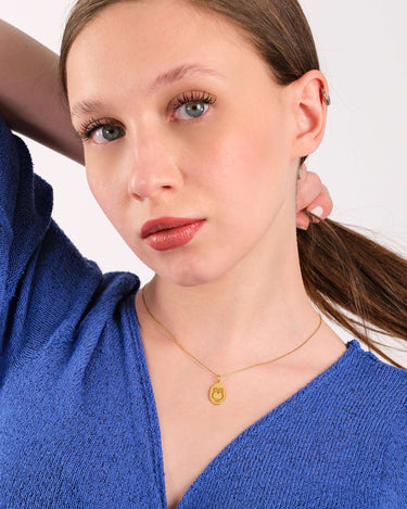 Young woman in a blue sweater looking at the camera, her 14K gold vermeil owl necklace visible.