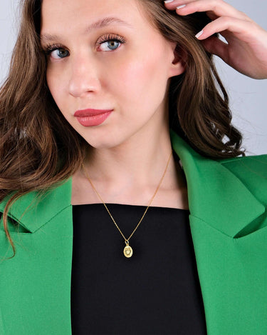 Close-up of a young woman wearing a gold owl pendant necklace, styled with a green blazer.