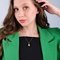 Close-up of a young woman wearing a gold owl pendant necklace, styled with a green blazer.