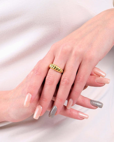 A woman&#39;s hands with manicured nails, one nail painted silver, wearing a 14k gold vermeil croissant ring on her right ring finger, against a light beige dress.