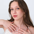 A woman with long brown hair and blue eyes posing with her hands near her face, highlighting the 14K solid gold daisy ring on her finger.