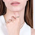 : A close-up of a woman&#39;s face, focusing on her lips and chin. She is lightly touching her lips with her hand, which is adorned with a gold evil eye ring featuring a blue gemstone.