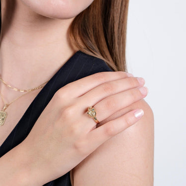 Close-up of a woman’s hand resting on her shoulder, showcasing the gold Ouroboros thumb ring with green gemstones.