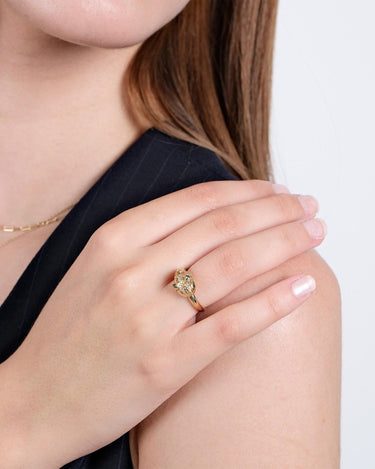 Close-up of a woman’s hand resting on her shoulder, showcasing the gold Ouroboros thumb ring with green gemstones.