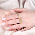 Close-up of two hands wearing rings, one with a gold bee design and honeycomb pattern.