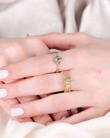 Close-up of two hands wearing rings, one with a gold bee design and honeycomb pattern.