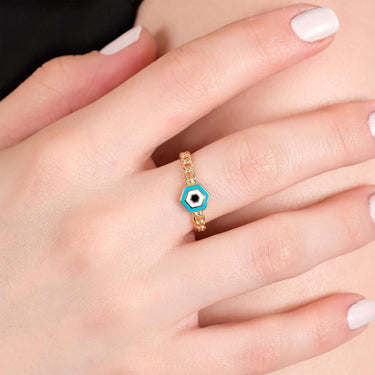 A close-up view of a hand with neatly manicured nails painted white, showcasing a gold chain ring with a hexagonal blue and white evil eye design.