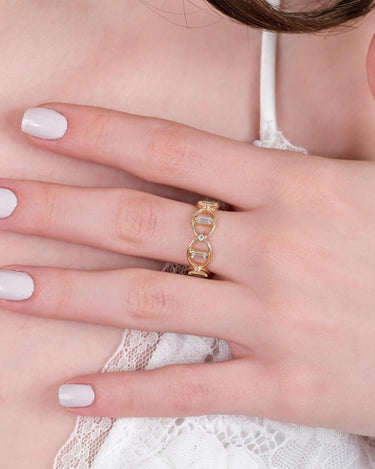 A close-up of a woman&#39;s hand with white nail polish, wearing a gold chain ring with rectangular gems and small round diamonds on her ring finger.