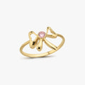 The Mionza Bow Ring, crafted in 14K solid gold, showcases a delicate bow design with a central small, round pink gemstone. The textured ring band features subtle ridges, adding an intricate touch to this elegant piece—perfect for symbolizing love and commitment.