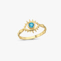 A gold ring featuring a spiky eye design with a blue gemstone at the center, displayed against a plain white background.