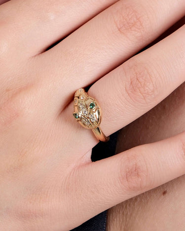 Close-up of a hand wearing a gold Ouroboros thumb ring with green gemstones as eyes