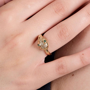 Close-up of a hand wearing a gold Ouroboros thumb ring with green gemstones as eyes