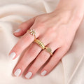 Close-up of a hand on a white fabric, wearing a gold flower ring with white enamel petals, and two additional gold rings.