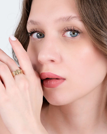 Woman with light makeup and wavy brown hair showcasing a gold bee ring with a honeycomb pattern on her finger.