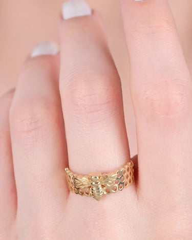 Close-up of a hand wearing a gold bee ring with a honeycomb pattern.