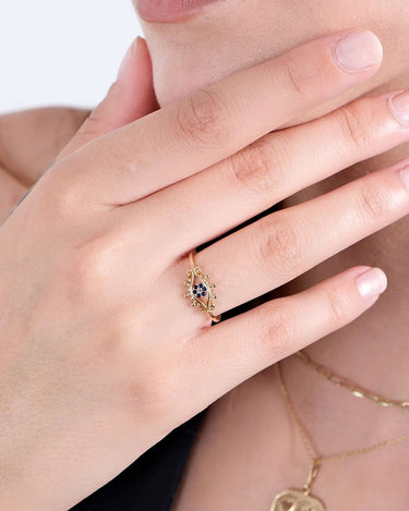 A close-up of a hand with manicured nails, wearing a gold evil eye ring with blue stones.