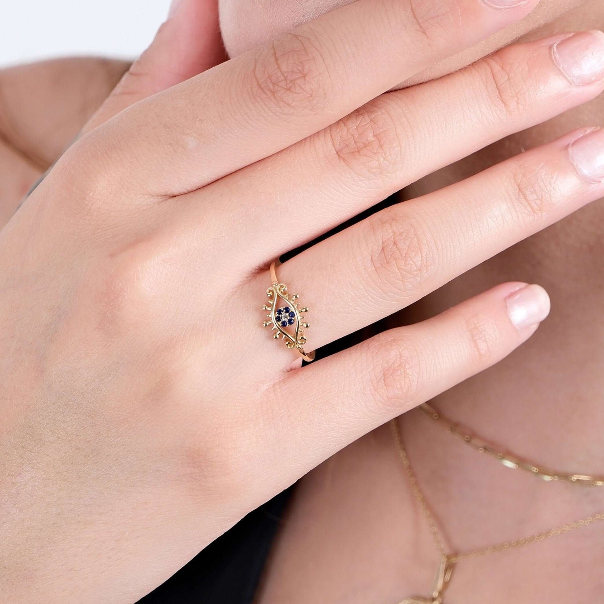 A close-up of a hand with manicured nails, wearing a gold evil eye ring with blue stones.