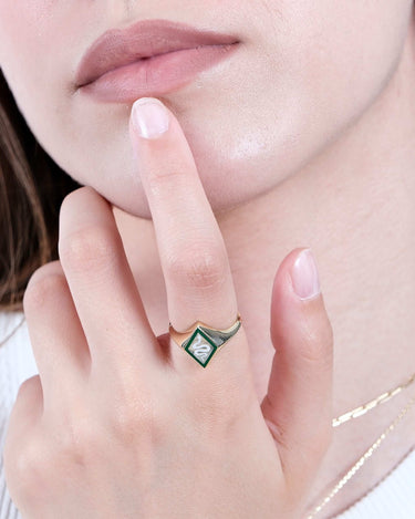 A close-up of a woman&#39;s face, focusing on her lips and chin, with her hand gently touching her chin. She is wearing a gold snake signet ring with a green and white enamel snake design.