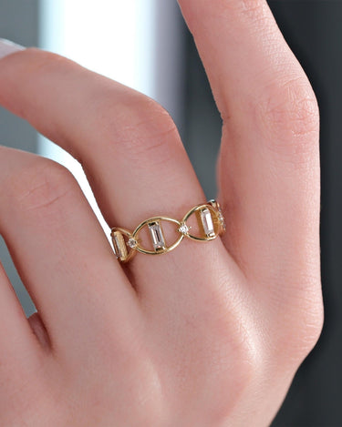 A hand with neatly manicured nails wearing Mionza's dainty Chain Ring in 14K solid gold, featuring two interlocking oval links embedded with diamonds, set against a blurred background.