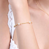 A close-up of a woman's arm wearing an elegant 18K gold vermeil bracelet adorned with evenly spaced white pearls, showcasing the delicate design against her smooth skin and lace-trimmed white fabric.