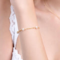 A close-up of a woman&#39;s arm wearing an elegant 18K gold vermeil bracelet adorned with evenly spaced white pearls, showcasing the delicate design against her smooth skin and lace-trimmed white fabric.