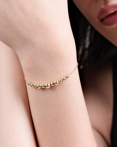 Close-up of a woman&#39;s wrist adorned with an 18K Gold Vermeil beaded bracelet featuring multiple small and large round beads arranged in a delicate pattern.