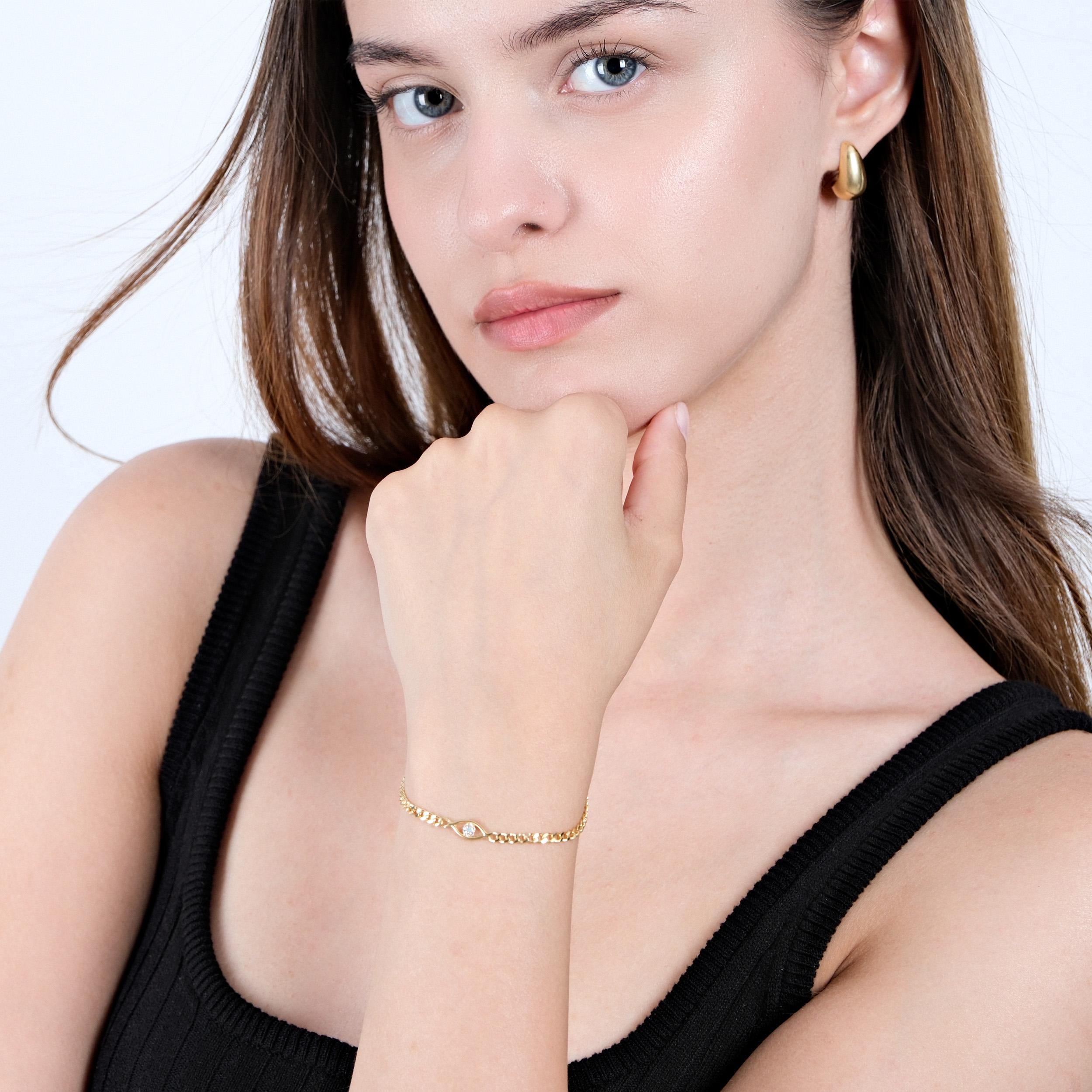 A woman with light skin poses with her hand near her chin, wearing an 18K Gold Vermeil Evil Eye Curb Chain Bracelet, with a focus on the bracelet's delicate design and gold finish.