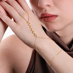 Close-up of a woman's hand resting on her cheek, showcasing a delicate gold snake hand chain bracelet draped across her hand, with a zigzag design as the central feature.