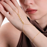 Close-up of a woman's hand resting on her cheek, showcasing a delicate gold snake hand chain bracelet draped across her hand, with a zigzag design as the central feature.