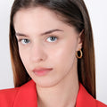 A woman in a red blazer, with long brown hair, wearing a medium-sized twisted hoop earring in 18K gold vermeil, looking directly at the camera.