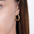 Close-up of a woman&#39;s ear wearing a medium-sized twisted hoop earring in 18K gold vermeil.