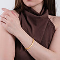 A close-up of a woman with crossed arms, wearing an 18K gold vermeil cuff bracelet on her right wrist, dressed in a brown top.