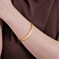 A close-up view of a person&#39;s arm wearing an 18K gold vermeil cuff bracelet against a brown fabric background.