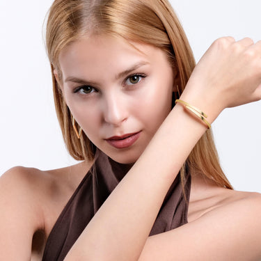 A woman with a focused expression shows off the 18K gold vermeil hinged bangle bracelet on her wrist, highlighting its elegant simplicity.