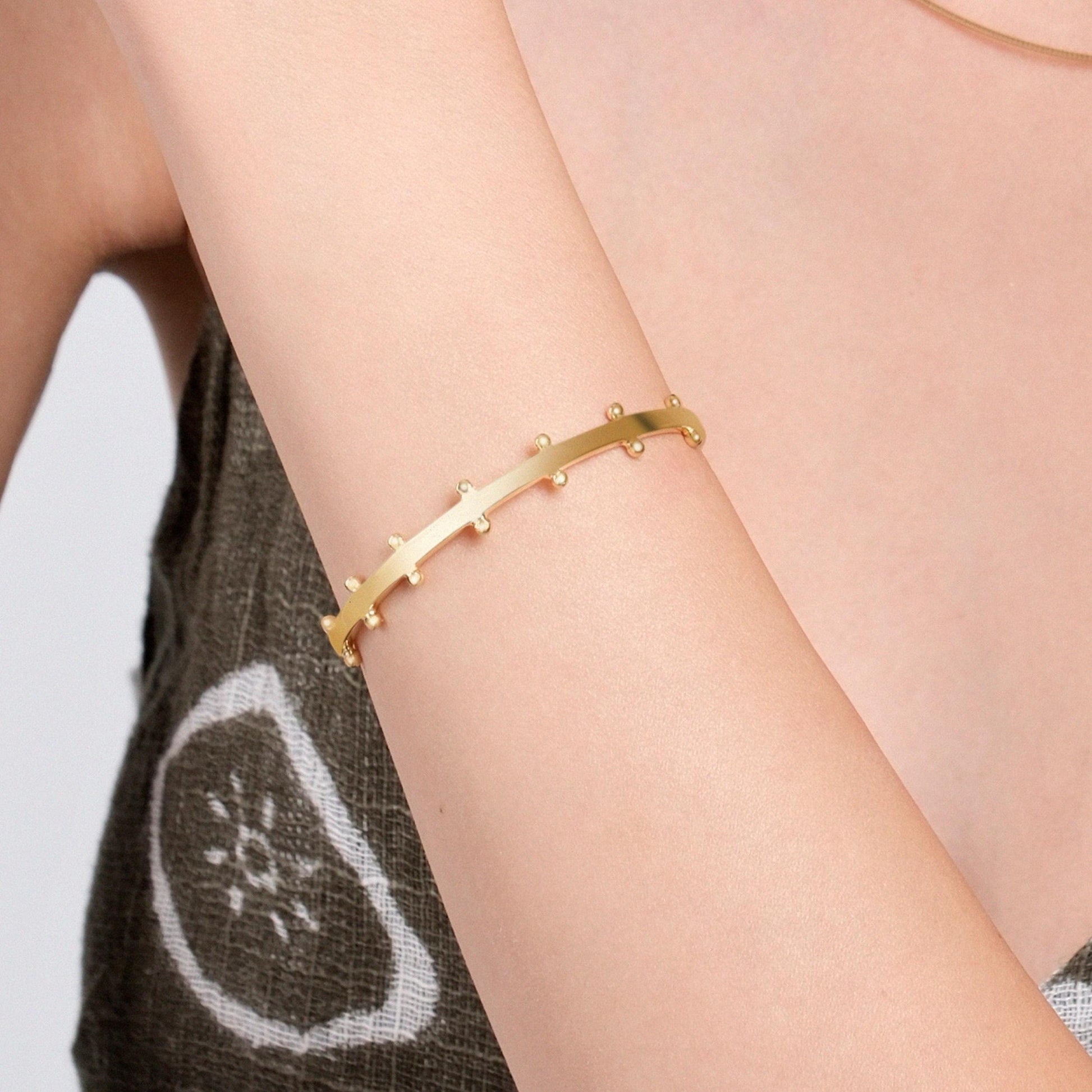 A close-up of a woman&#39;s arm adorned with an 18K gold vermeil station cuff bracelet.