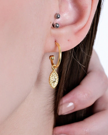 Close-up of an ear wearing a gold hoop earring with a North Star and evil eye charm.