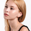 Woman wearing an 18K gold vermeil twist ear cuff in her upper ear, with minimal makeup and smooth blonde hair.