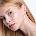 Close-up of a woman wearing a twisted gold vermeil ear cuff. She gazes off to the side, with her blonde hair neatly parted and draped over her shoulder.